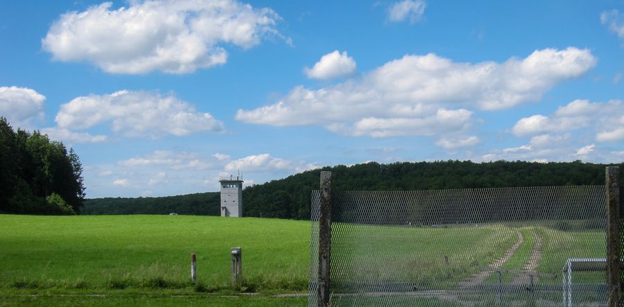 Zaunreste im Vordergrund und ein Wachturm inmitten grüner Landschaft gehen auf die frühere innerdeutsche Grenze zurück